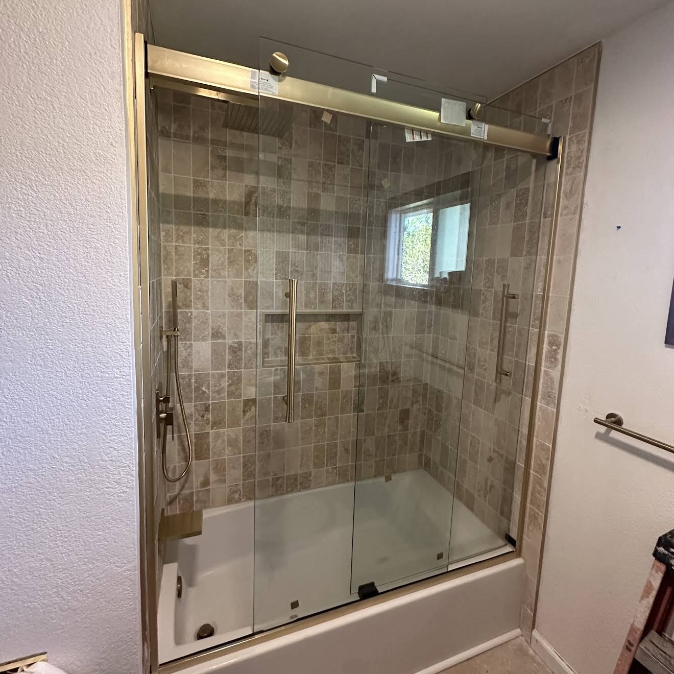 The finished shower — frameless glass with brushed brass hardware.
